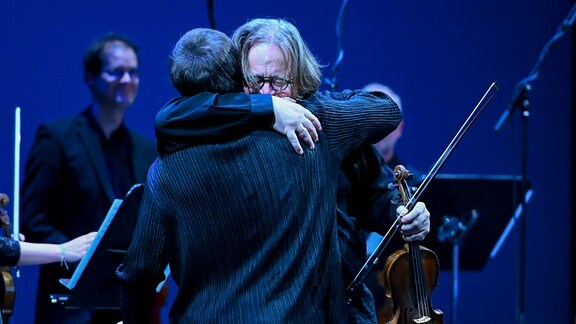 Zwei Mitglieder eines Orchesters umarmen sich.