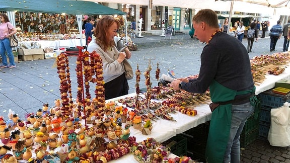 Ein Verkäufer an einem Stand mit verschiedenen Zwiebeln spricht mit einer Kundin
