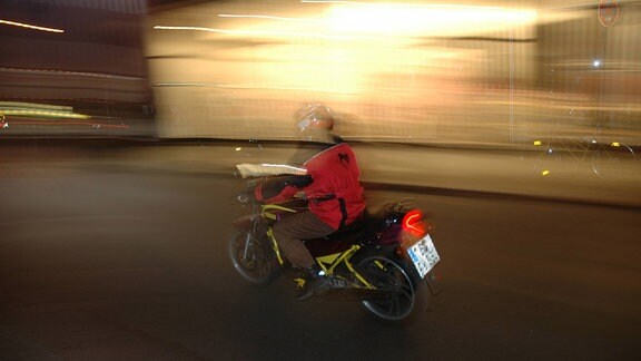 Eine Person auf einem Moped bei Nacht fotografiert mit viel Bewegungsunschärfe
