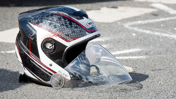 Ein beschädigter Motorradhelm liegt nach einem schweren Verkehrsunfall auf einer Straße.