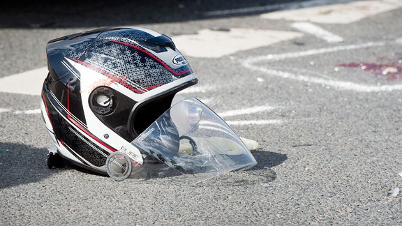 Ein beschädigter Motorradhelm liegt nach einem schweren Verkehrsunfall auf einer Straße.