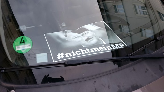 Hinter einer Auto-Frontscheibe liegt ein bearbeitetes Kemmerich-Foto mit der Aufschrift #nichtmeinMP