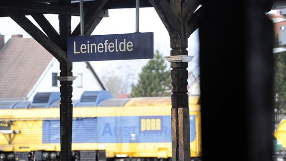 Das Bahnhofsschild für den Bahnhof Leinefelde ist an einem Holzdach befestigt.