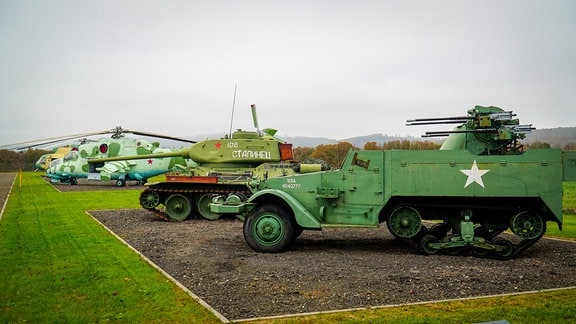 Auf einer Wiese stehen Militärfahrzeuge wie Hubschrauber und Panzer.