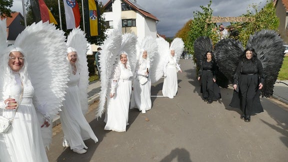 Links im Bild sind fünf als weiße Engel verkleidete Frauen, rechts im Bild zwei als schwarze Engel verkleidete Frauen.