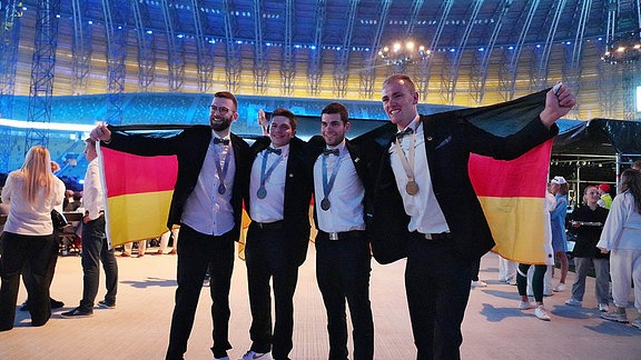 Vier Männer mit einer Deutschlandfahne, triumphieren mit Medaillen.