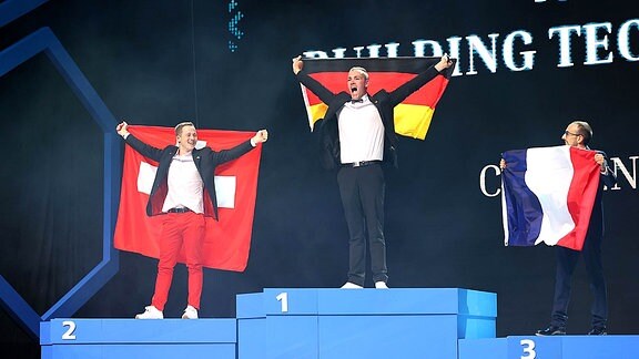 Drei Männer stehen auf einem Siegerpodest, Lauhoff mit deutscher Fahne in der Mitte.