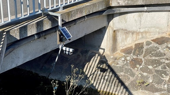 Ein Messgerät ist an einer Brücke über einem Fluss angebracht.
