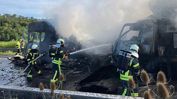 Feuerwehrleute löschen zwei rauchende Lkws auf einer Autobahn.