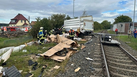 Feuerwehrleute und aufgerissene pakete liegen neben einer Bahnstrecke.