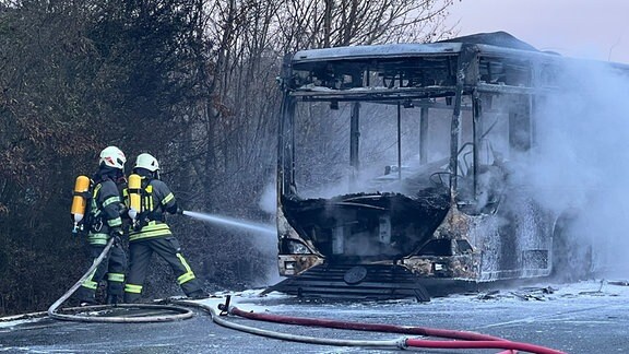 Zwei Feuerwehrmänner löschen einen brennenden Bus