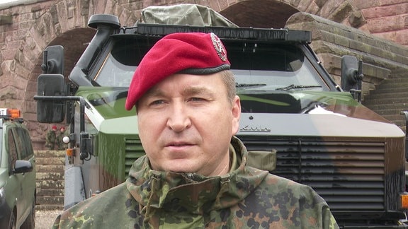 Ein Bundeswehrsoldat steht vor einem Geländewagen.