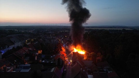 Ein brennendes Haus im von oben fotografiert, die Flammen lodern noch.