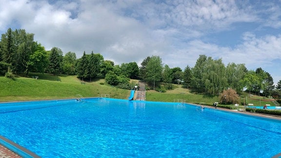 Ein Blick über das Schwimmbad Oldisleben mit Rutsche und Sonnensegeln.