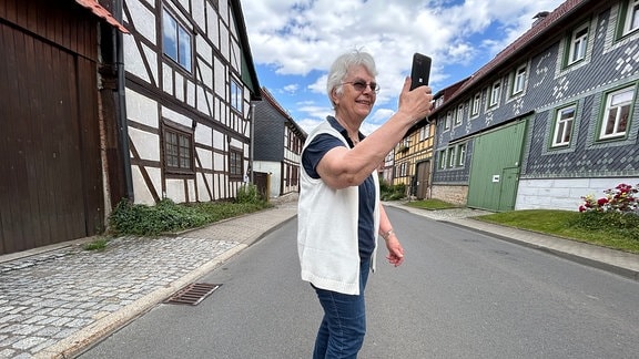 Eine Frau hält auf einer Straße ein Handy in die Höhe.