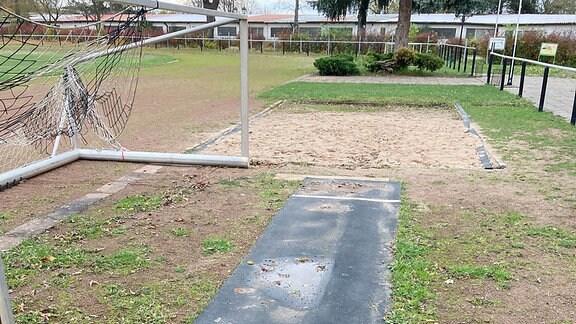 Ein Fußballtor steht neben einer Anlaufbahn zu einer Weitsprungrube.