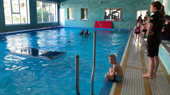 Kinder während des Unterrichts am Rande eines Schwimmbeckens.