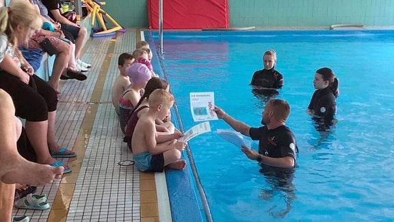 Kinder während des Unterrichts am Rande eines Schwimmbeckens.