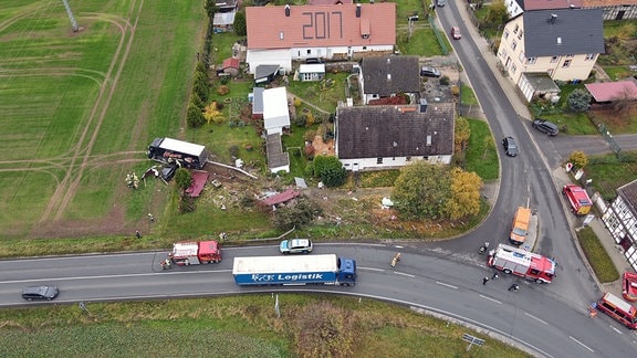 Ein Lkw steht nach einem Unfall auf einem Feld. In einem Graten hinter ihm ist eine Schneise der Verwüstung. Neben dem Lkw steht ein Auto. Es ist nach einem Zusammenprall zerstört. Auf dem Dach des Autos liegt ein Wellblech.