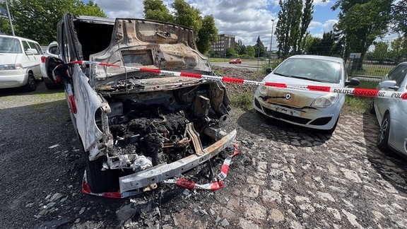 Zwei verbrannte Autos hinter einer Polizeiabperrung