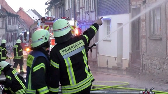 Feuerwehrleute löschen Häuser in einer Straße.