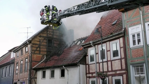 Feuerwehrleute löschen einen Brand im Dachstuhl eines Hauses aus einem Leiterwagen.