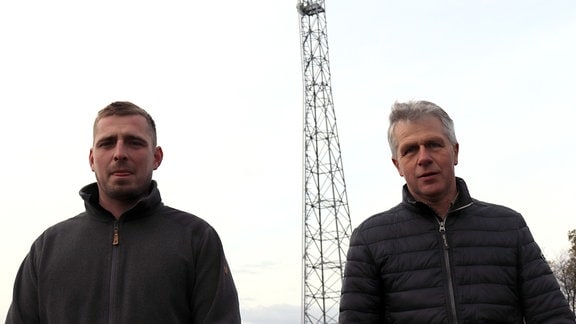 Zwei Männer stehen vor einem Mobilfunkmast.