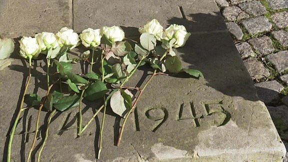 Weiße Rosen liegen nebeneinander, daneben die Zahl 1945 in Stein geschlagen.