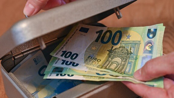 Eine Frau nimmt Eurobanknoten aus einer kleinen Geldkassette.
