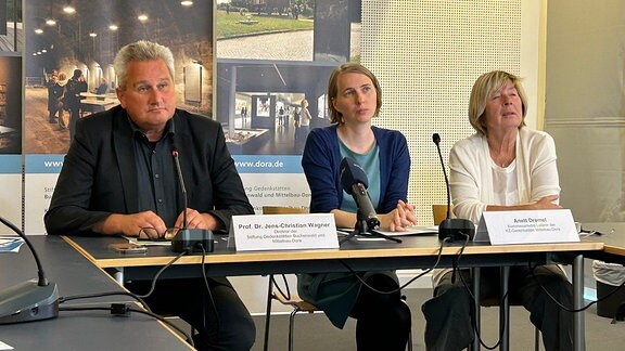 Ein Mann und zwei Frauen bei einer Pressekonferenz.