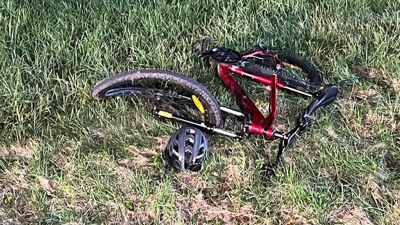 Ein rotes Fahrrad liegt auf einer Wiese, daneben ein Helm.