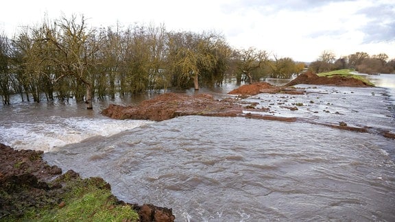 Wassermassen fießen durch die Deichöffnung am Fluss Helme auf die umliegenden Flächen.