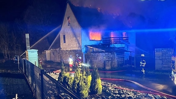 Feuerwehrleute löschen ein brennendes Haus.