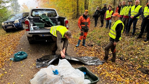 Männer hantieren mit Plastiksäcken im Wald vor 