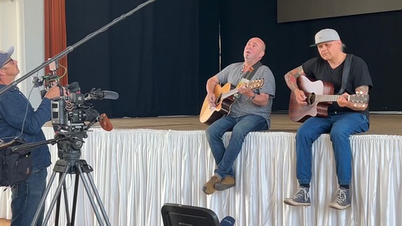 Zwei Männer sitzen am Bühnenrand und spielen Gitarre.