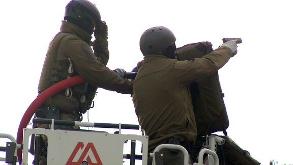 SEK-Beamte mit Pistole und Wasserschlauch im Korb einer Feuerwehr-Drehleiter.