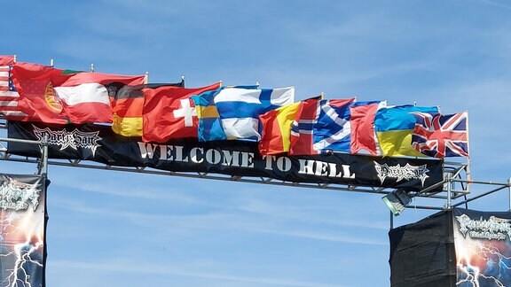 Flaggen mehrerer Länder wehen über dem Einlass zu einem Festivalgelände.