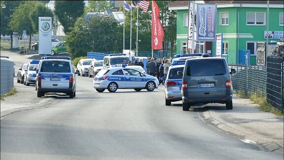Auf einer Straße vor einem Autohaus stehen mehrere Polizeifahrzeuge und Personen