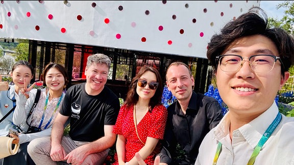Sechs Menschen sitzen vor dem weißen Gartenpavillion in Chengdu und machen ein Selfie. Mit dabei: Alexander Glasner und seine Frau.
