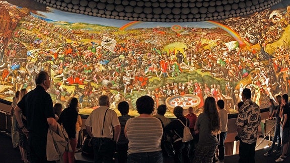 Viele Besucher blicken zu einem riesigen Panoramabild empor, das eine detailreiche Szene zeigt