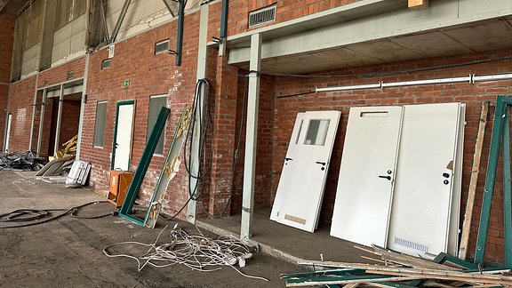 Mehrere weiße Türen lehnen in einer Halle an einer Backstein-Wand umgeben von Baumaterialien