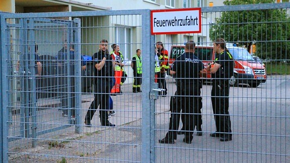 Polizisten und Rettungssanitäter stehen vor einer Flüchtlingsunterkunft