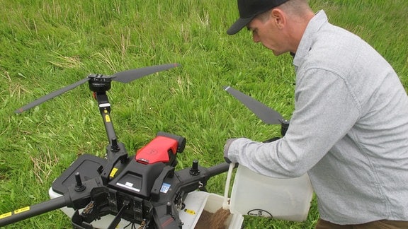 Robert Baum füllt Samen in eine Behälter an einer Drohne