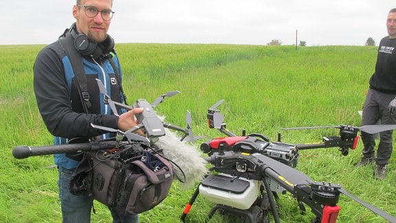 Kamera Assistent Benjamin Klieme hält eine kleine Drohne zum Vergleich neben die Landwirtschaftdrohne