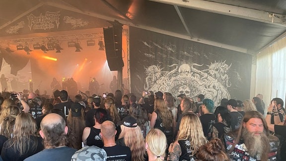 Heavy-Metal-Fans stehen in einem großen Zelt vor einer Bühne.