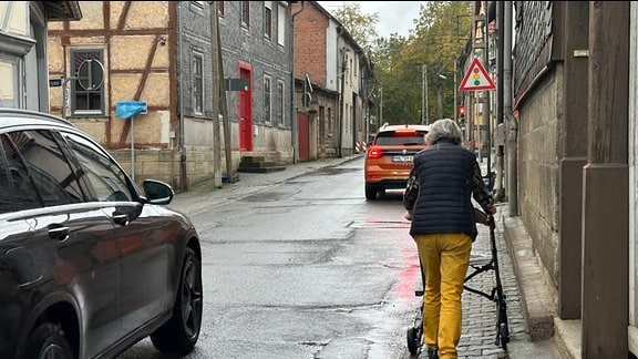 Eine ältere Frau läuft mit Rollator auf einem Gehweg.