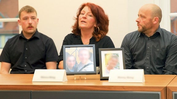 Drei Menschen sitzen hinter Fotos in Bilderrahmen