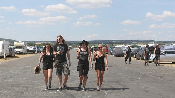 Vier Metalfans gehen über ein Festival-Gelände.