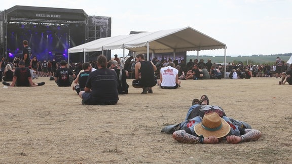 Ein Mann mit Hut ruht sich auf einem Festivalgelände aus.