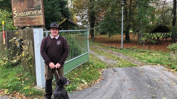 Ein Mann steht mit seinem Hund vor einem Schild.
